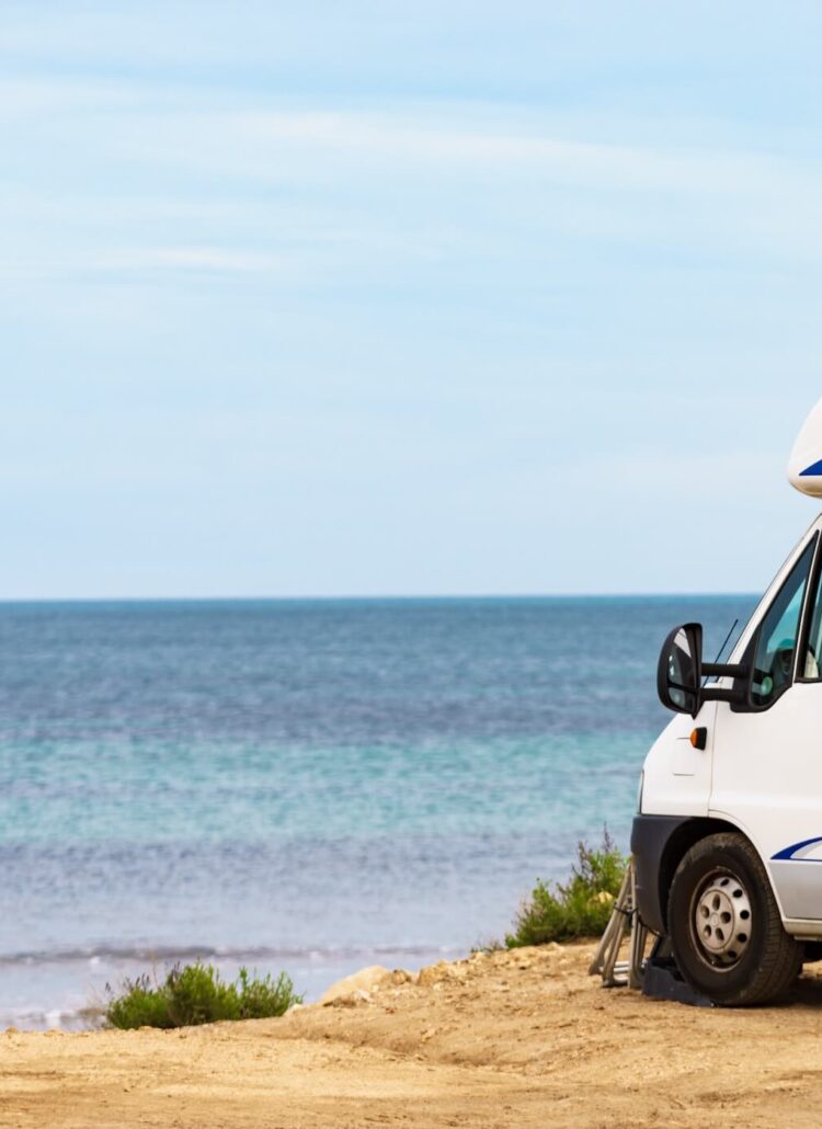 Een witte camper staat geparkeerd op gele rotsen, op de achtergrond blauwe zee. Een camperreis door Puglia.