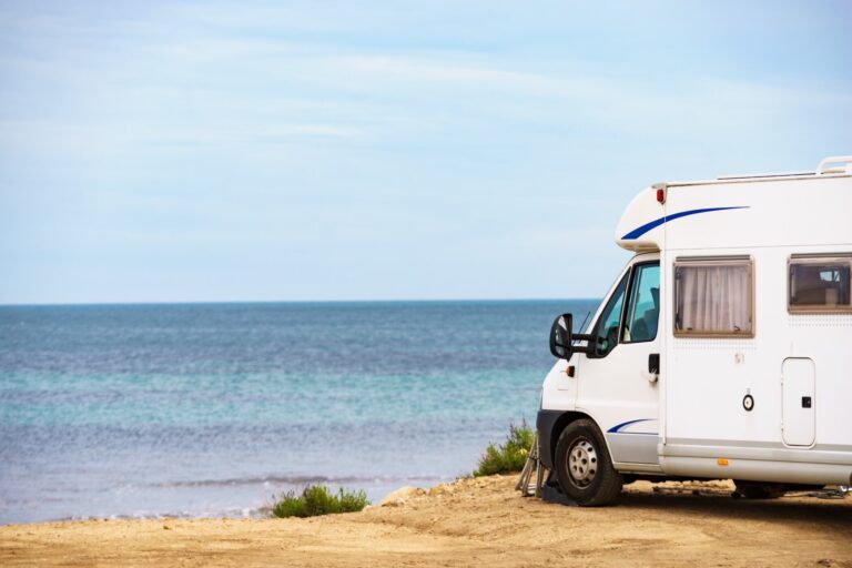 Een witte camper staat geparkeerd op gele rotsen, op de achtergrond blauwe zee. Een camperreis door Puglia.
